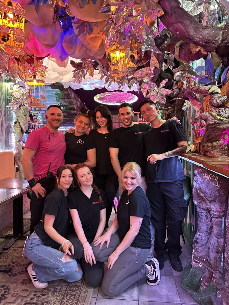 Fotografía del equipo de Serendipia posando sonriente bajo decoraciones encantadas de árboles y luces mágicas.